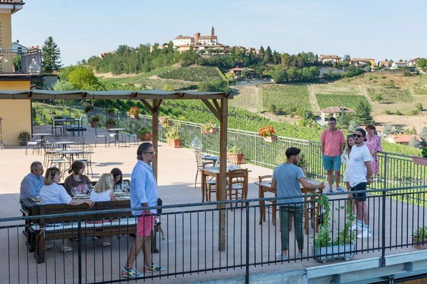 Una terraza con gente cenando, un viñedo al fondo y una colina con edificios. 5
