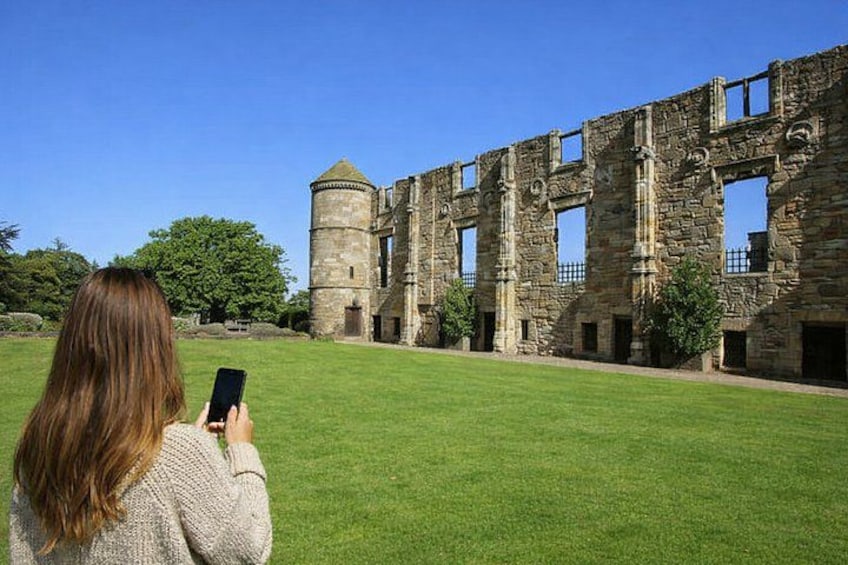 A person taking a photo of a historic stone building with a tower. 1
