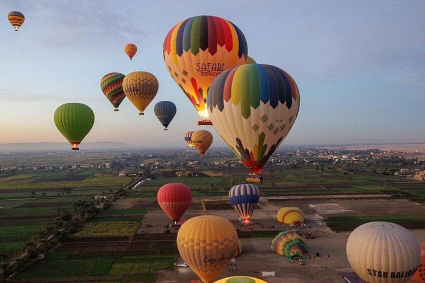 A hot air balloon festival with multiple colorful balloons in the air over a rural landscape. 1