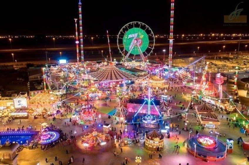 A brightly lit amusement park at night with a Ferris wheel, various rides, and a large crowd. 5