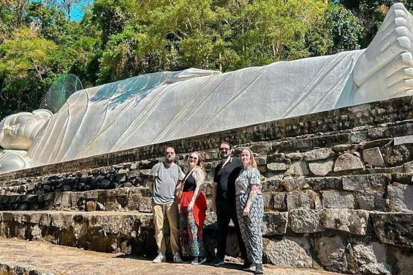 A group of people standing in front of a stone wall with a large, covered structure behind them. 4