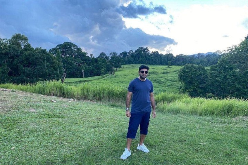 A person standing in a grassy field with trees and hills in the background. 3