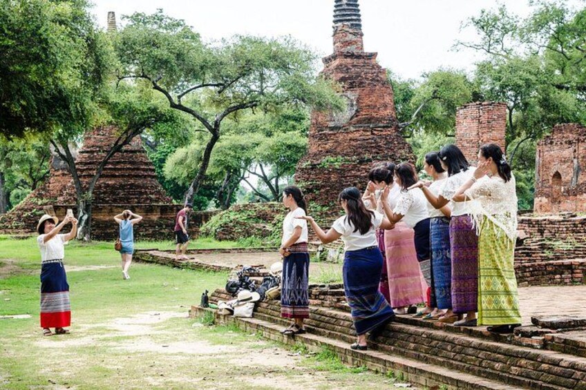 Un grupo de personas vestidas con atuendo tradicional de pie en los escalones de un templo, con antiguas estructuras de ladrillo y árboles al fondo. 4