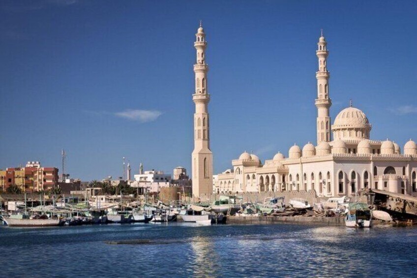 En moské med två minareter och kupoler, en småbåtshamn med båtar och en klarblå himmel. 5