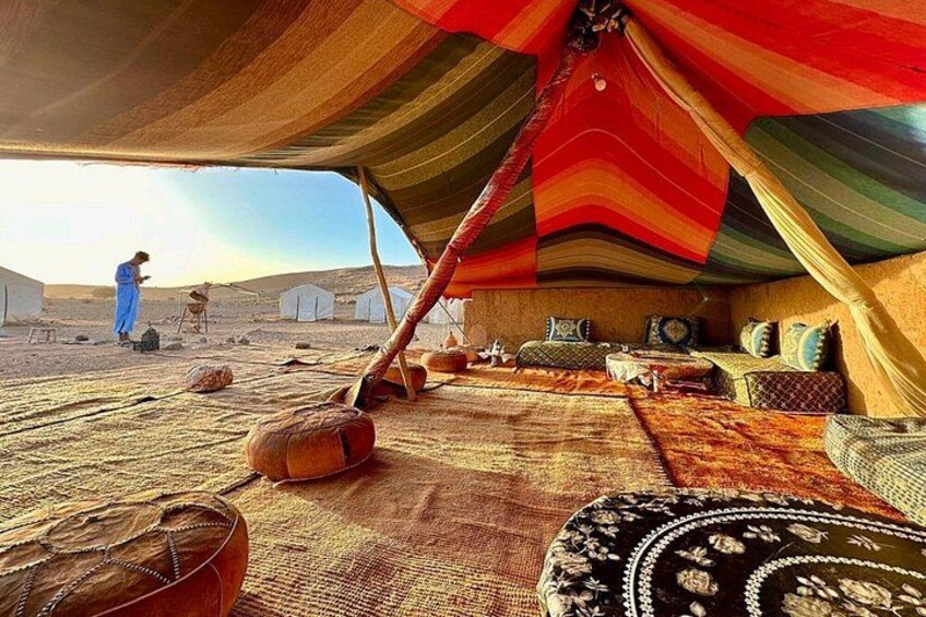 A tent with colorful fabric, cushions, and a woven rug in a desert setting. 1