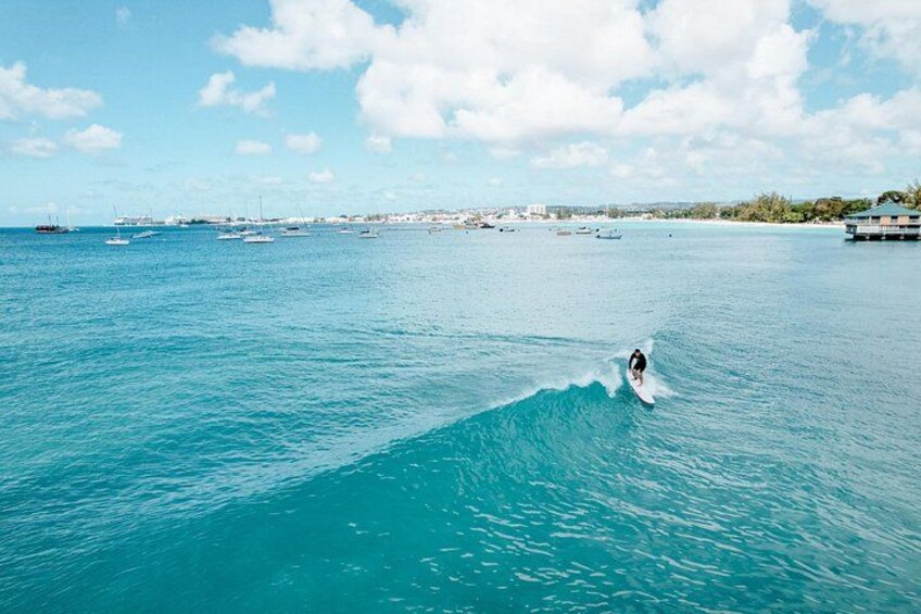 A person surfing on a clear blue sea with boats in the background. 4
