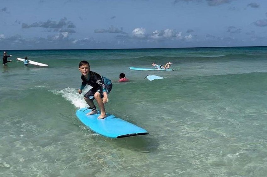 A person surfing in clear shallow water with other surfers in the background. 1