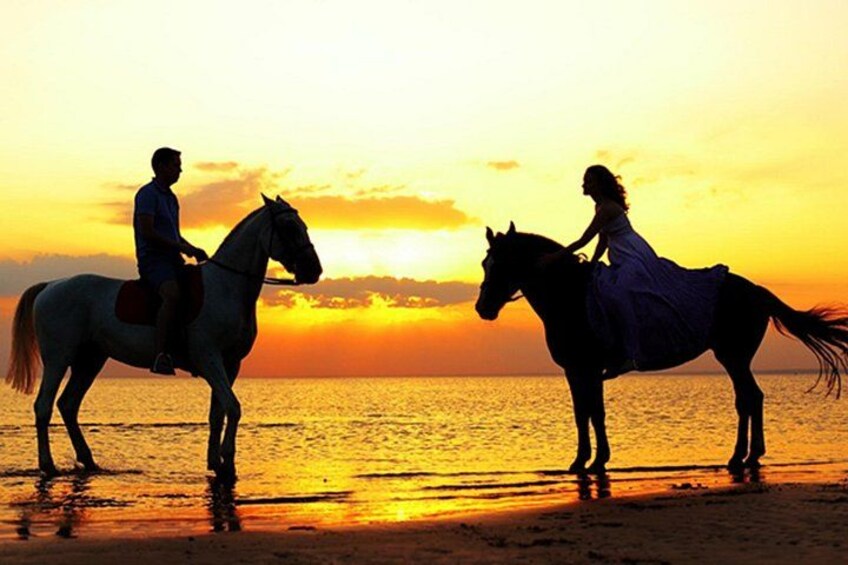 Due persone cavalcano a cavallo su una spiaggia al tramonto. 3