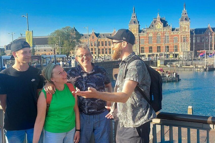 Een groep mensen staat langs een waterkant, met historische gebouwen op de achtergrond. 4