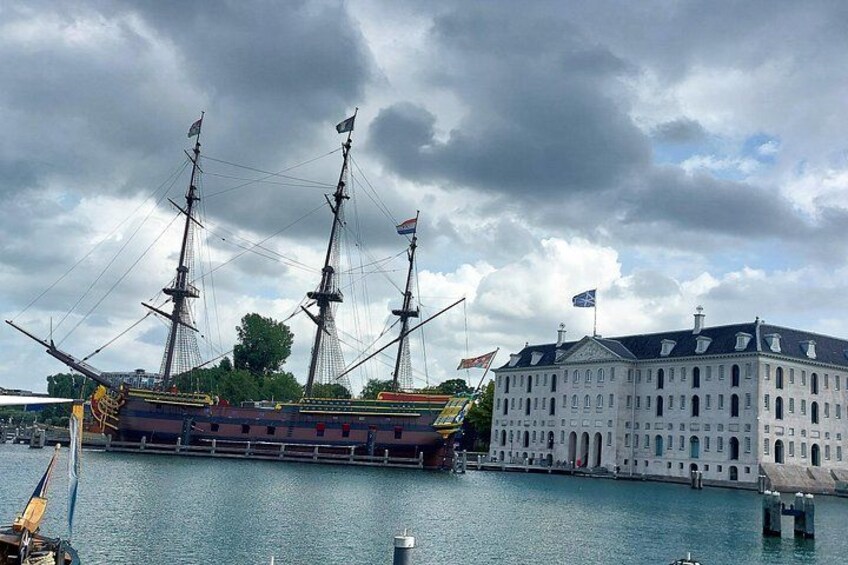 Een historisch schip in de haven, met een groot wit gebouw in de buurt. 3
