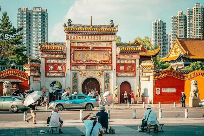 A traditional gate with intricate designs, surrounded by modern buildings and a busy street with pedestrians and vehicles. 2