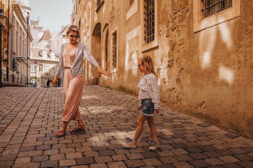A cobblestone street with historic buildings, a person walking with a child, and a clear sky. 2