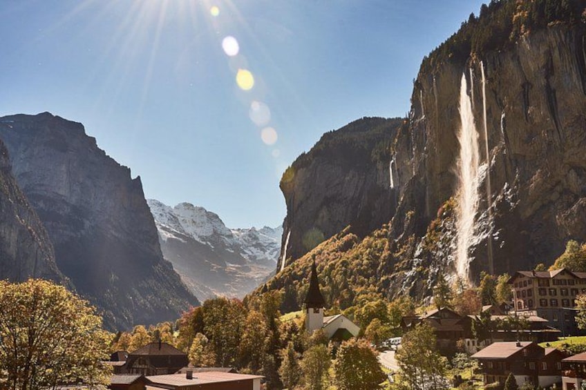 A mountainous landscape with a waterfall, buildings, and trees. 2