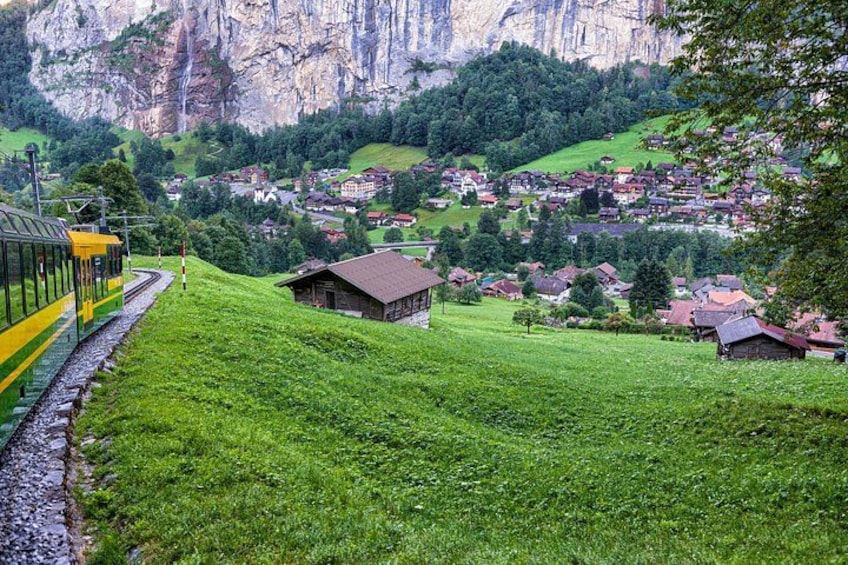 A train on tracks, a green hillside, and a village with buildings in the valley. 3