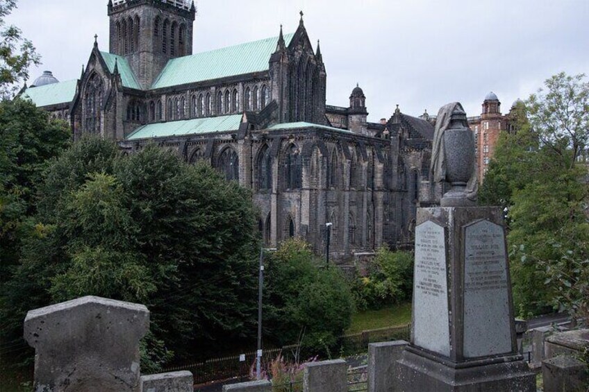 A Gothic-style church with a green roof, surrounded by trees and a stone monument. 1