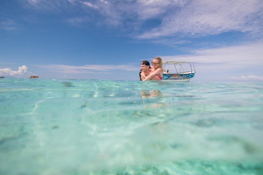 A couple in a boat on clear turquoise water, with a small boat in the background. 4