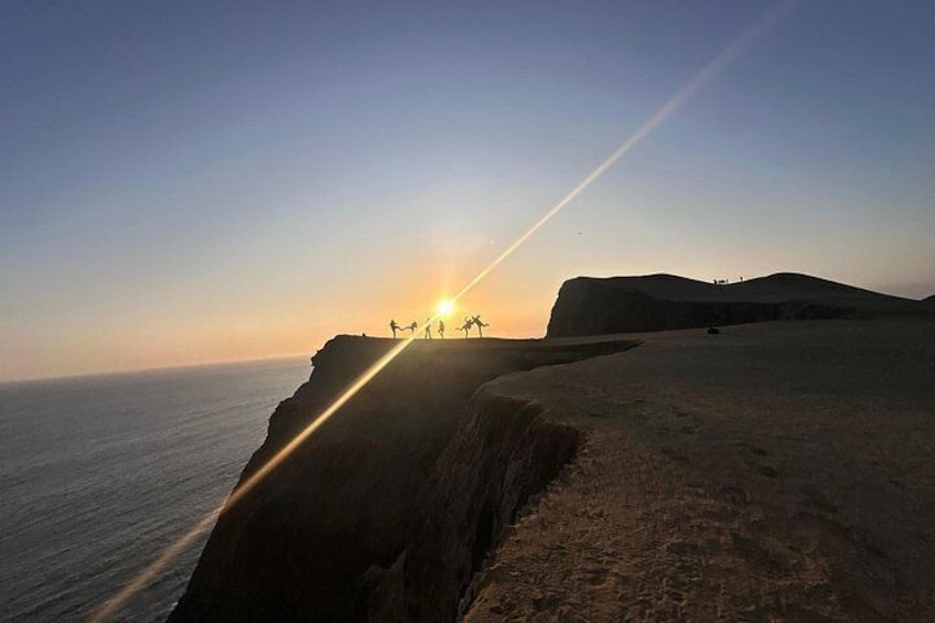 Un atardecer sobre un acantilado costero, con siluetas de personas contra el cielo. 3