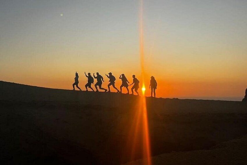 Een groep mensen wandelt over een heuvel tijdens de zonsondergang. 2