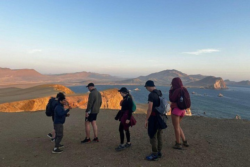 Un grupo de personas de pie en un sendero de tierra con vistas a un paisaje costero con montañas y acantilados. 2