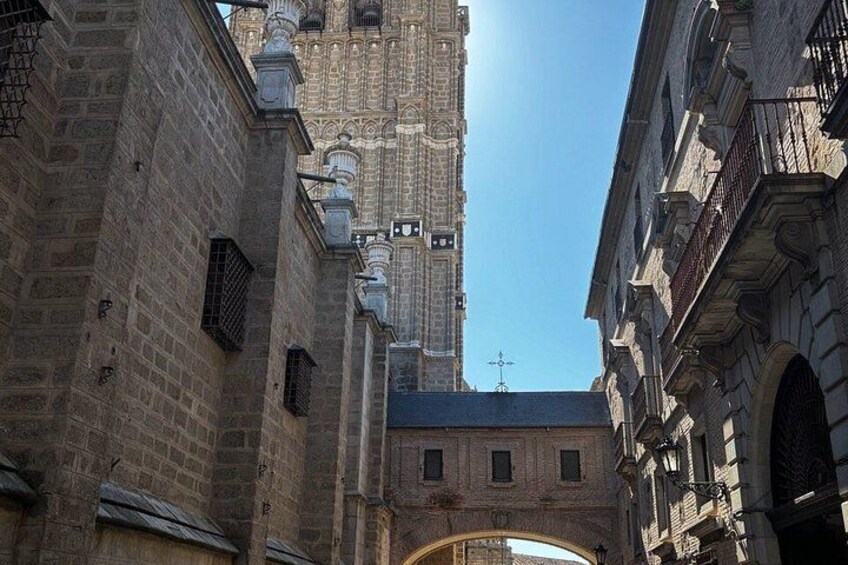 Un estrecho callejón con edificios históricos de piedra, una alta torre con detalles intrincados y un cielo azul despejado. 4