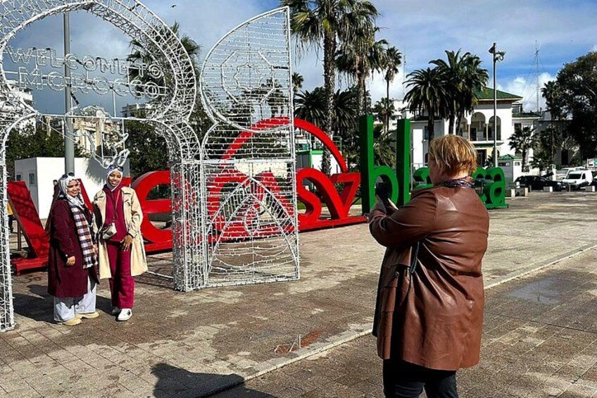 A metal gate with a red 'Welcome' sign, palm trees, and a building in the background. 1