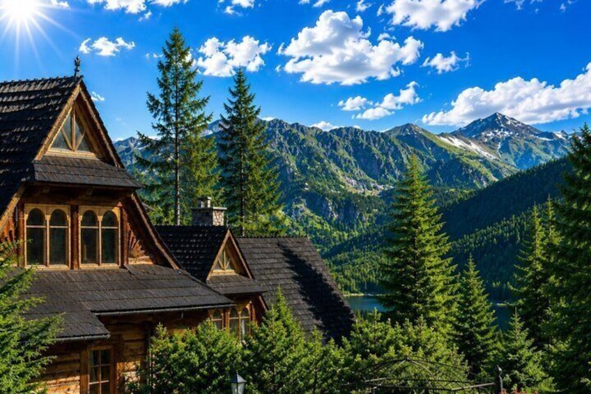 A mountain cabin with a steep roof, surrounded by evergreen trees and a lake. 2