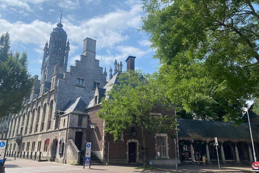 A historic building with a clock tower, a tree-lined street, and a clear blue sky. 3