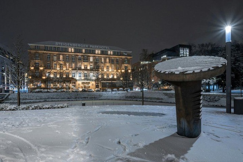Een park bedekt met sneeuw, met een grote stenen sculptuur en een hotel op de achtergrond. 3