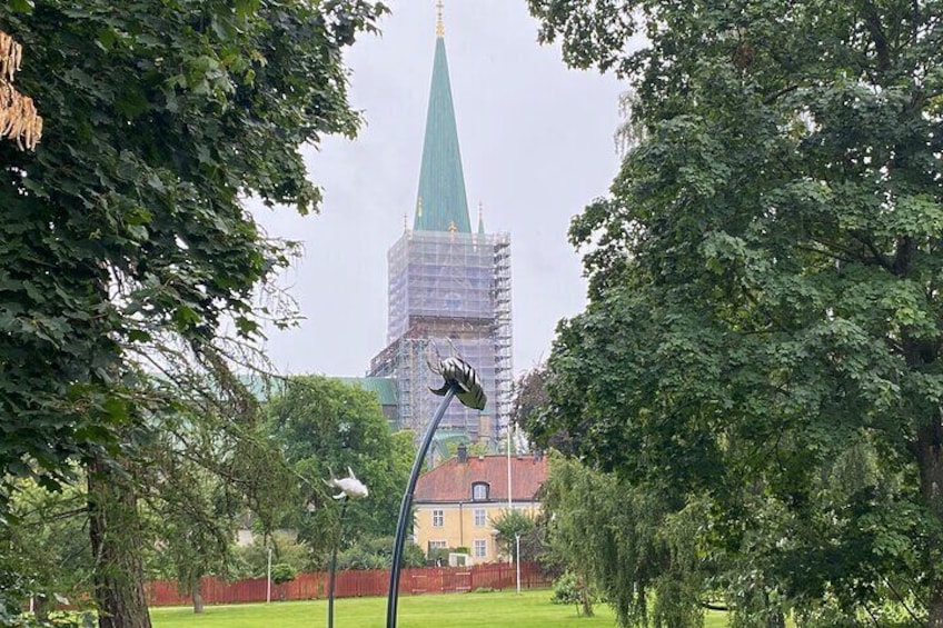 A park with trees, a street lamp, and a building with a green spire under construction. 1