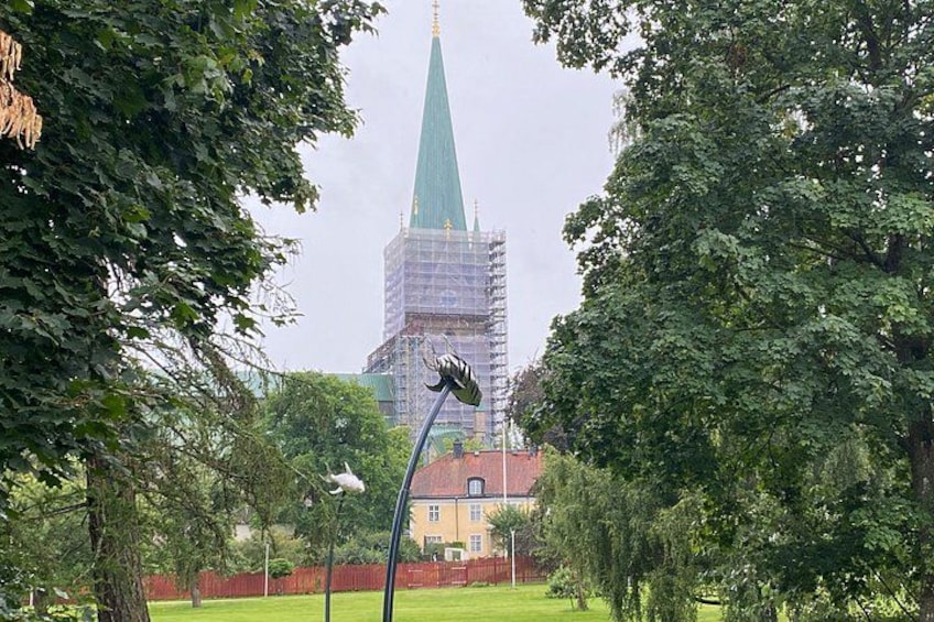 En park med en gatlykta, träd och en byggnad med ett grönt torn som är under uppförande. 4