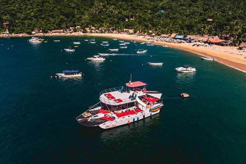 A large boat with a red and white color scheme docked near a beach with several smaller boats and a sandy shore lined with palm trees. 4