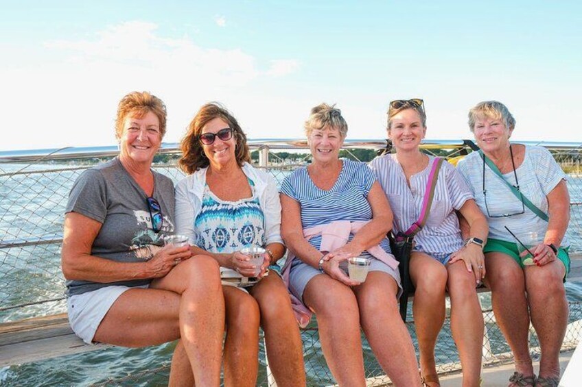 Five people sitting on a boat with a body of water and a bridge in the background. 5