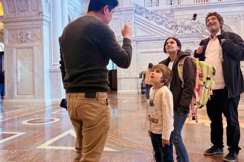 A man taking a photo of a group of people in a grand hall with marble floors and ornate columns. 2