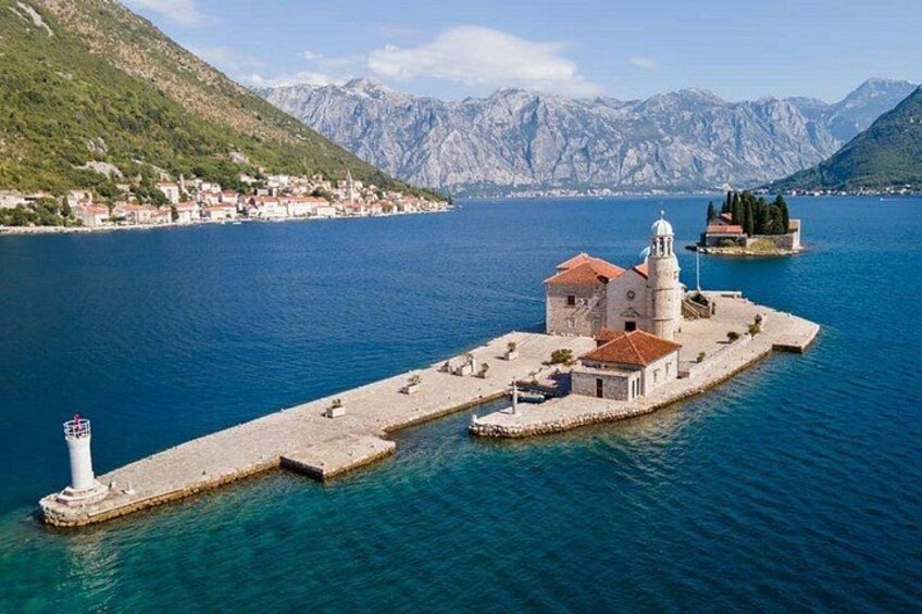 Un pueblo costero con una iglesia destacada en una pequeña isla, rodeado de montañas y un mar azul cristalino. 5