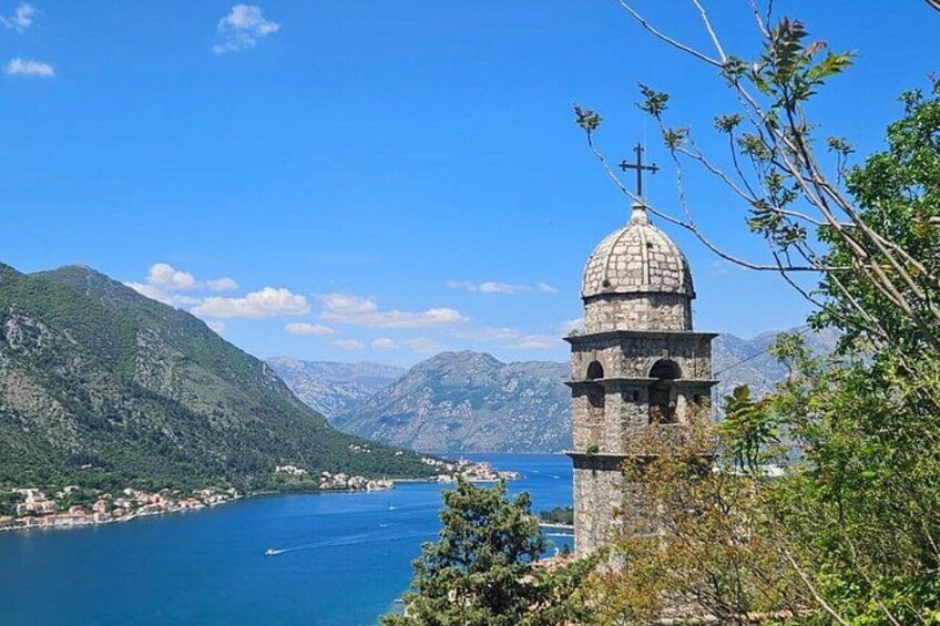 Una torre de piedra con cúpula y cruz, con vistas a un lago rodeado de montañas. 1