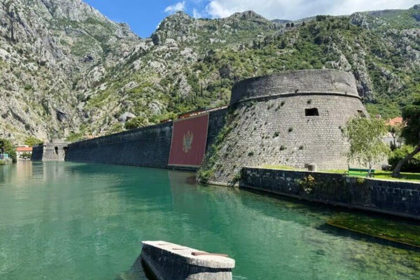 Una fortaleza de piedra histórica junto a un lago turquesa cristalino, rodeada de montañas escarpadas. 5
