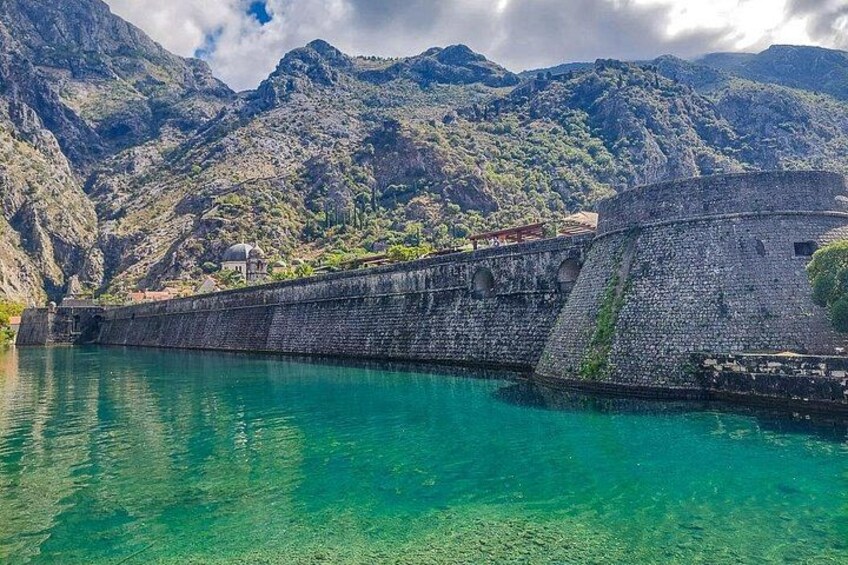 Una fortaleza de piedra junto a un lago turquesa con montañas al fondo. 3