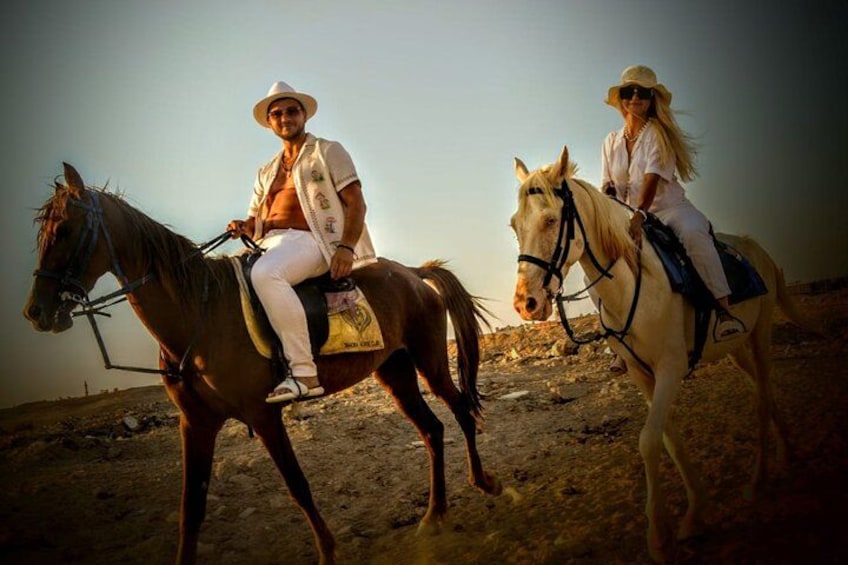 Two people riding horses in a desert landscape. 1