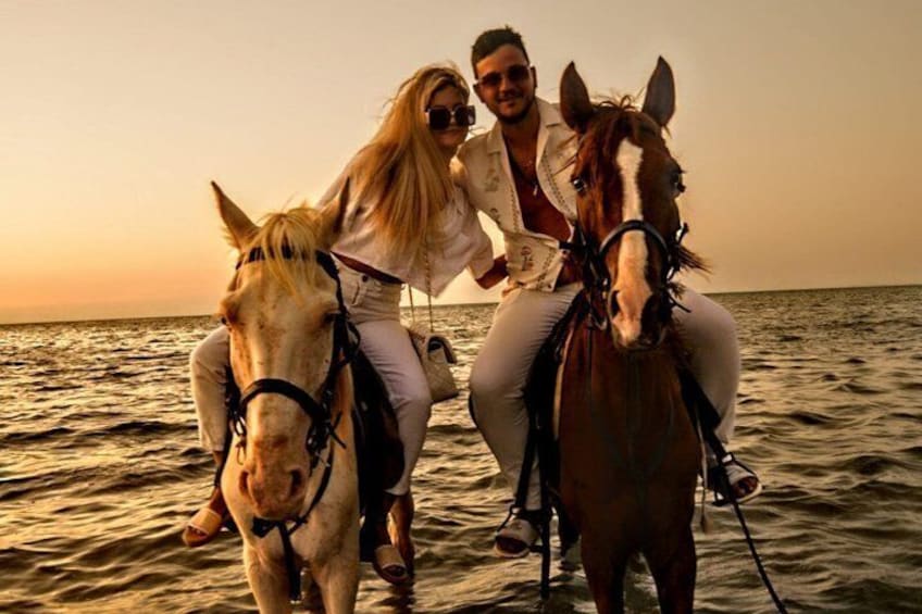 Two people riding horses on a beach at sunset. 4