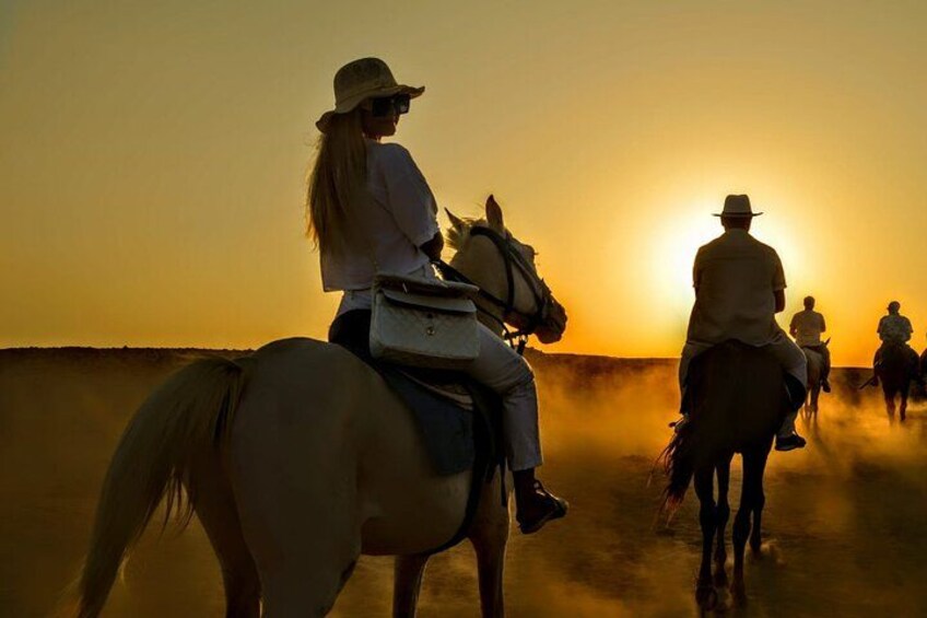 A group of people riding horses on a flat terrain during sunset. 2