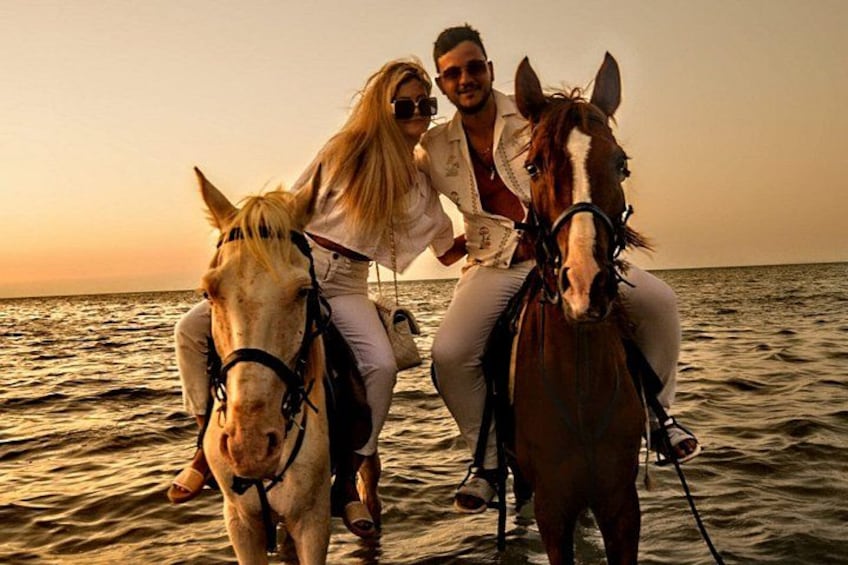 Due persone cavalcano cavalli su una spiaggia al tramonto. 4