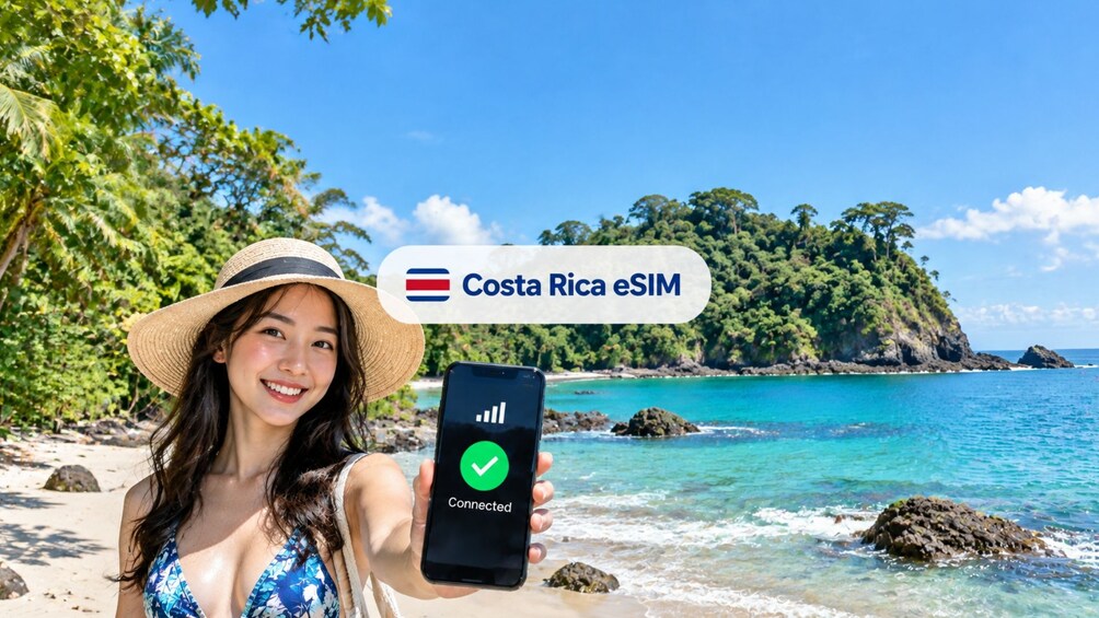 Iemand houdt een smartphone vast met een eSIM-logo, staand op een strand met helder turquoise water en rotsachtige uitstulpingen. 1