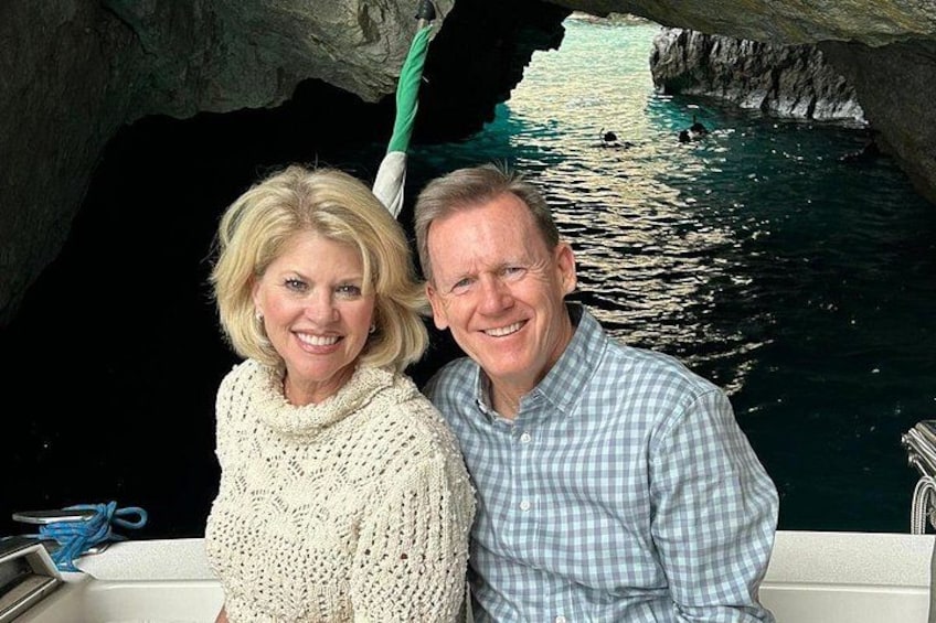 Two people on a boat near a rocky cave entrance with water. 2