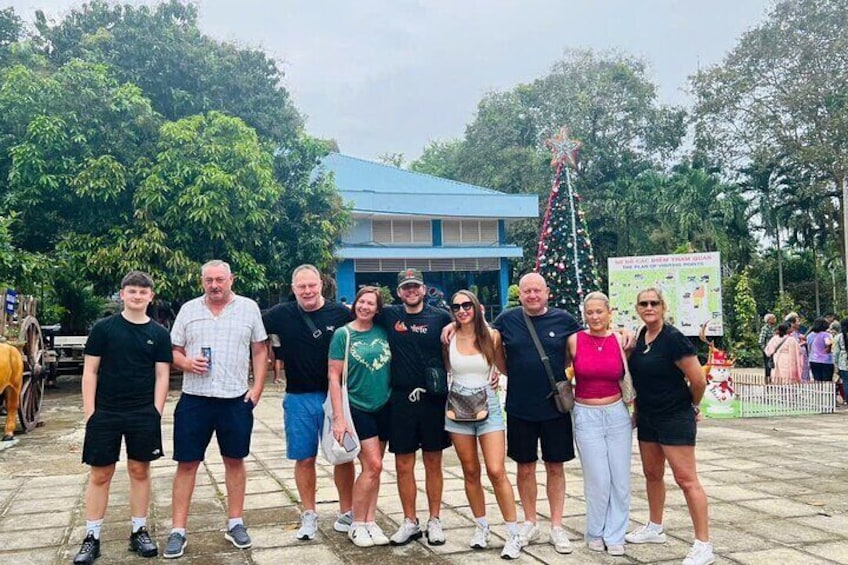 Un grupo de personas posando frente a un edificio con techo azul y un árbol de Navidad decorado. 3
