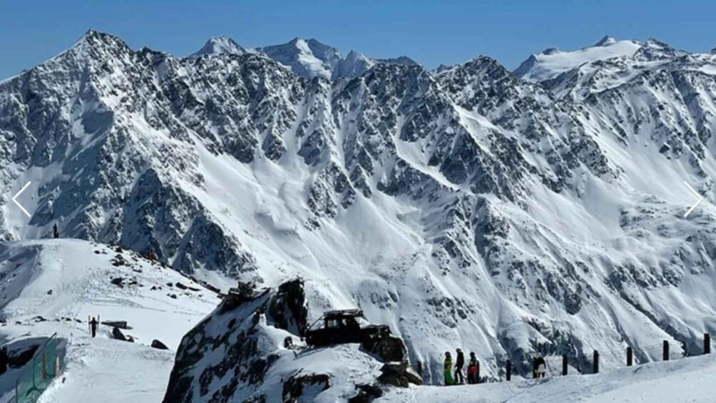 A snow-covered mountain range with a group of people standing at the base. 1