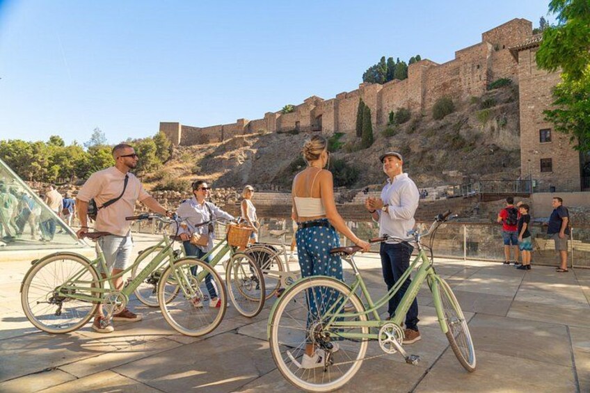 People standing near bicycles, a historical building, and a clear sky. 1