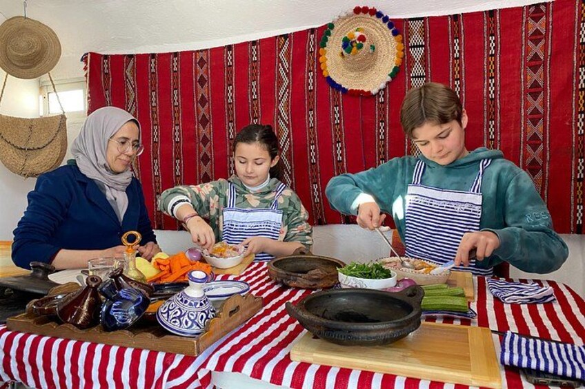 Three people preparing food at a table with striped cloths and traditional textiles in the background. 2
