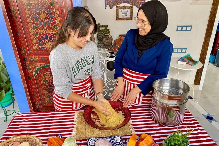 Two people preparing food at a table with a red and white striped tablecloth, a patterned wall, and a decorative door in the background. 4