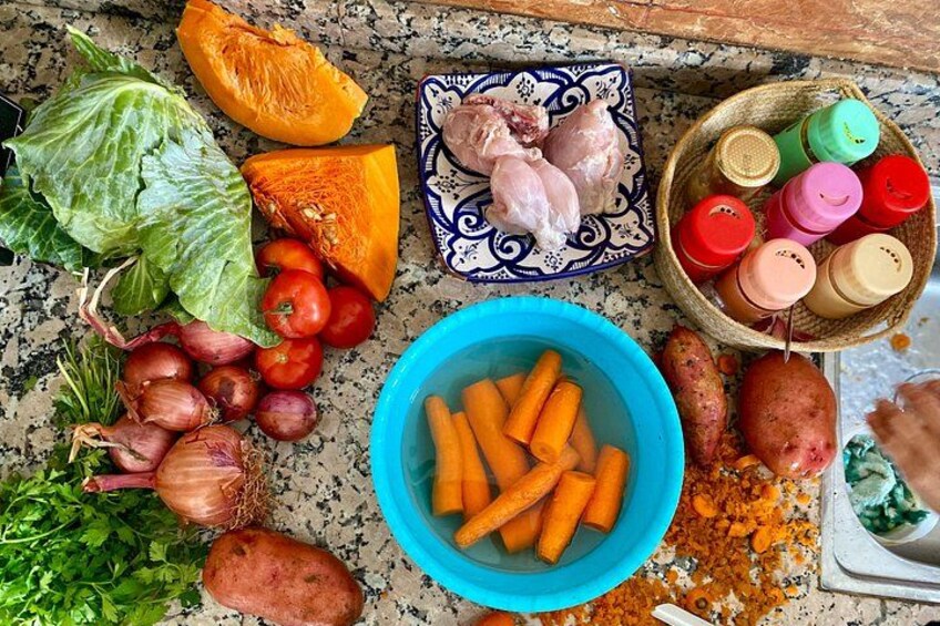 A kitchen counter with various vegetables, a bowl of carrots, and a plate of chicken. 3