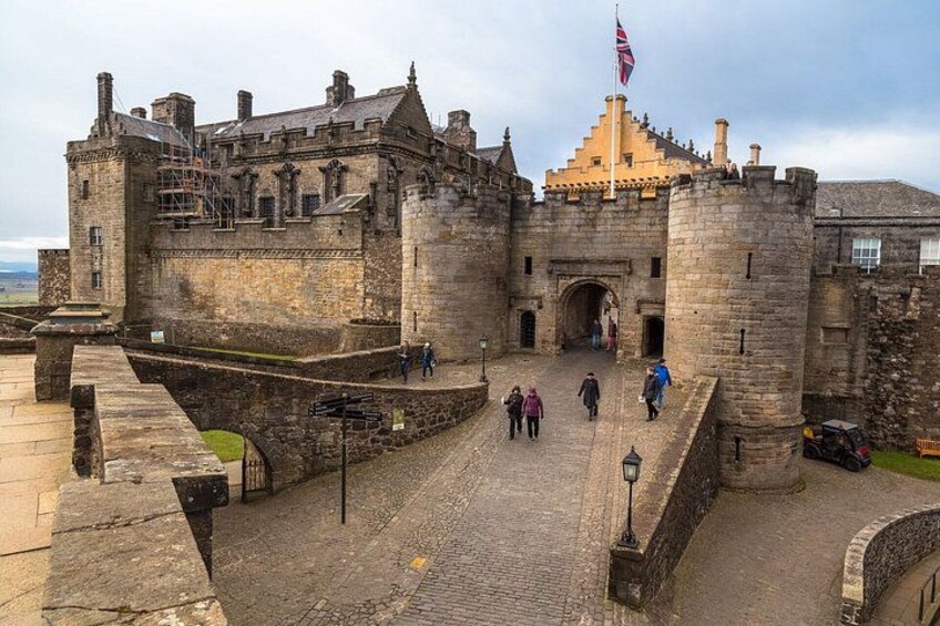 Un château de pierre historique, orné d’un drapeau, avec une entrée pavée et quelques personnes qui s’y promènent. 4